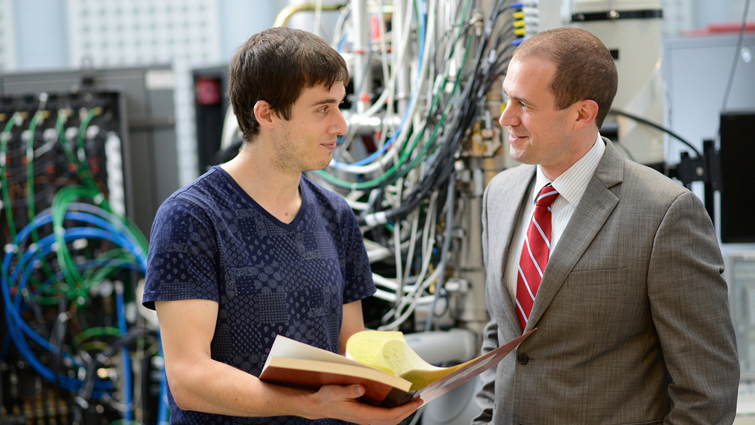 A student and a man in a suit talk in front of a computer server with lots of wires