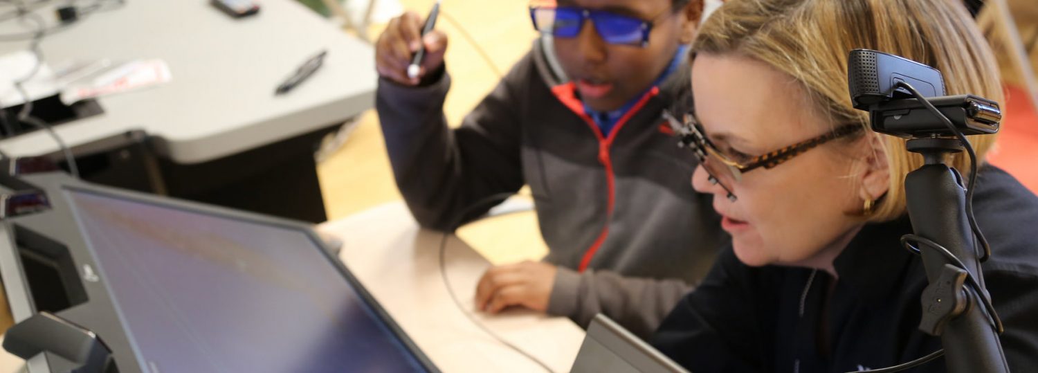 A teacher and student look at a screen while the student holds a pointer pen