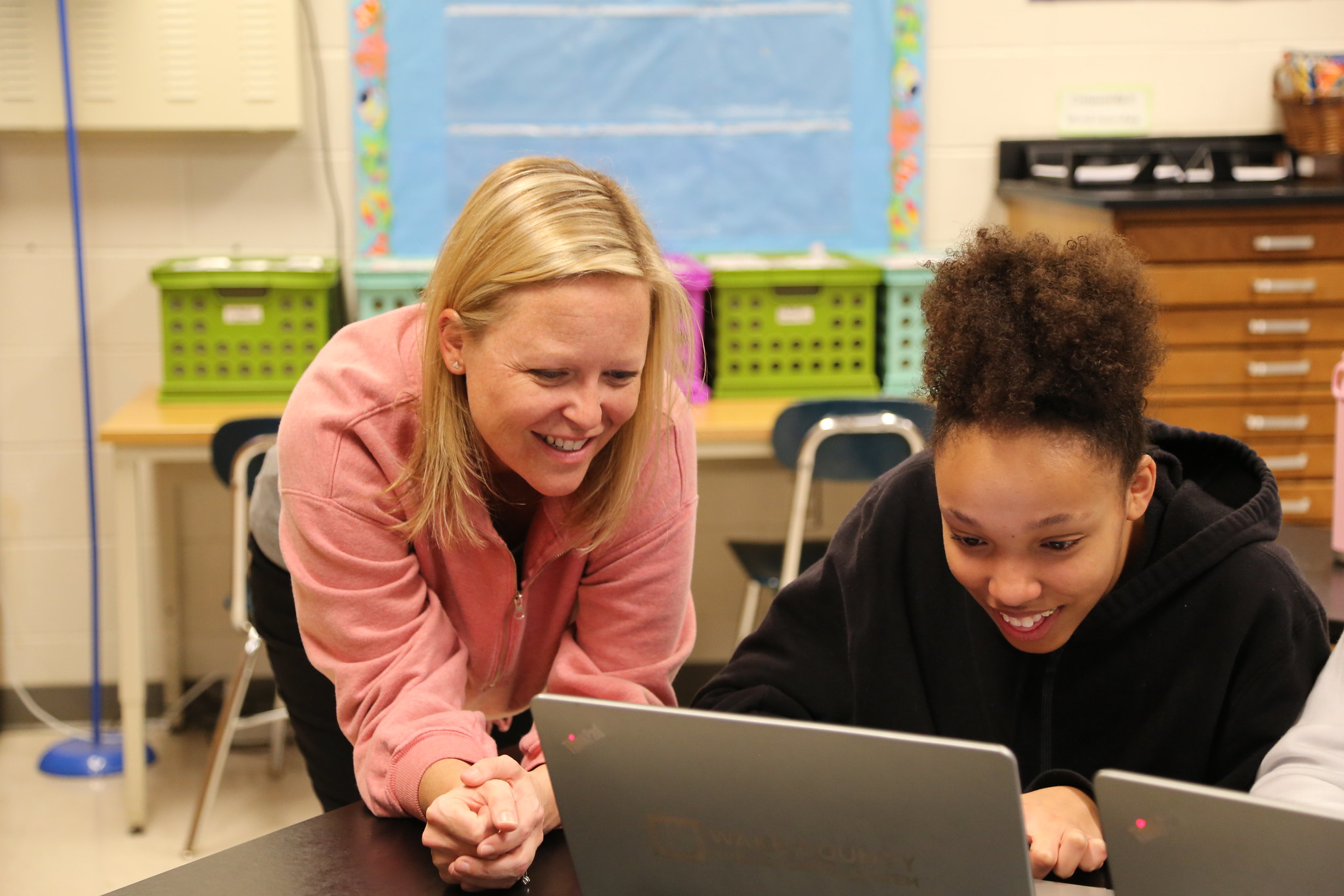 A teacher and student work together in front of a laptop in a classroom