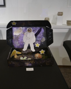 A painted black box featuring an astronaut in a space suit walking around an outer space environment with stars and rocks.