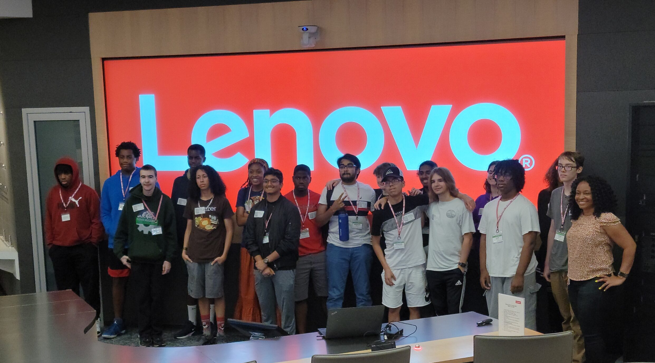 A group of high school students stand in front of a screen that shows the Lenovo logo