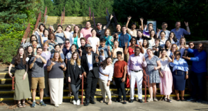 A large group of 50+ professional scholars post on the steps of an outdoor space with trees surround them