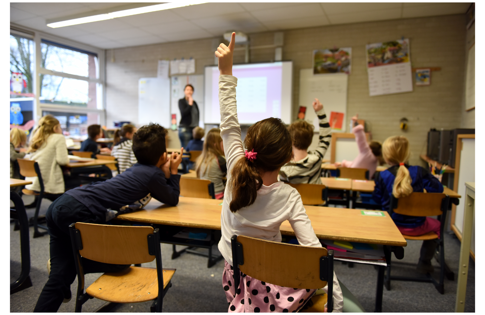 A girl in the back of a classroom raises her hand