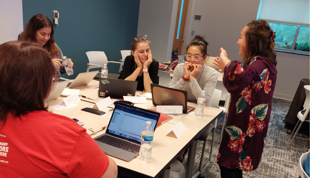 Senior Research Scholar and HI-RiSE Co-Director  Gemma Mojica talks with a group of educators and data scientists at a table in front of laptops