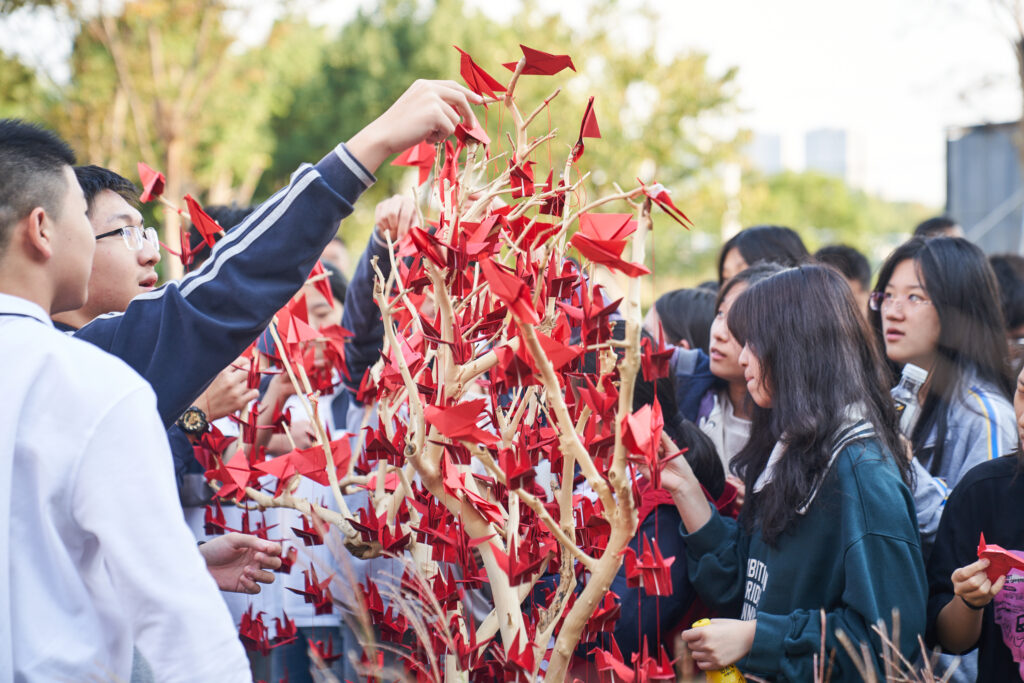 A group of students surround a tree filled with red origami hummingbirds
