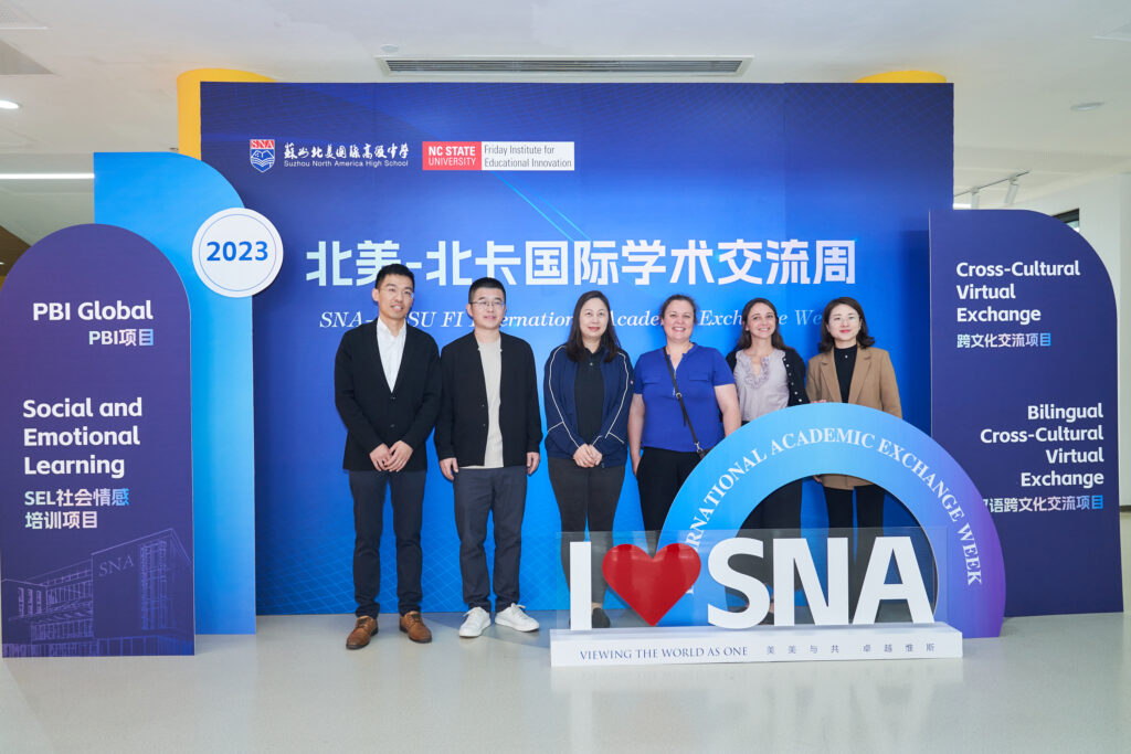 A group of educators in front of a large graphic 3-D sign that says I Love SNA, PBI Global, Social and Emotional Learning, Cross-Cultural Virtual Exchange in both English and Mandarin