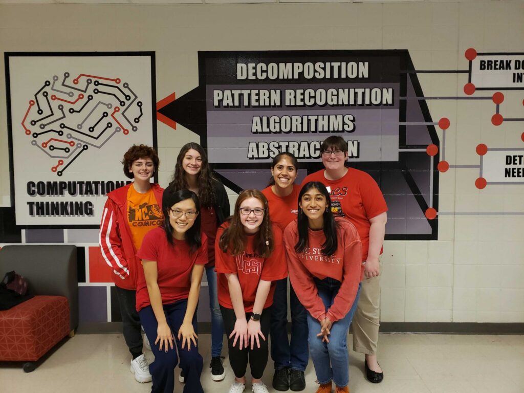 A group of students post in a cluster in front of a wall featuring a computational thinking map graphic.