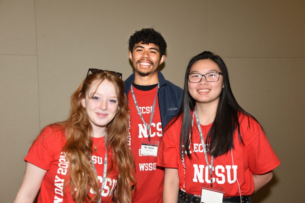 Three students in matching red shirts featuring "NCSU" stand in a group wearing red, white and blue medals.
