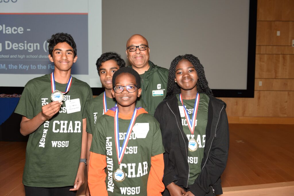 A group of students in green shirts with "CHAR" prominently feature wear red, white and blue medals around their necks.