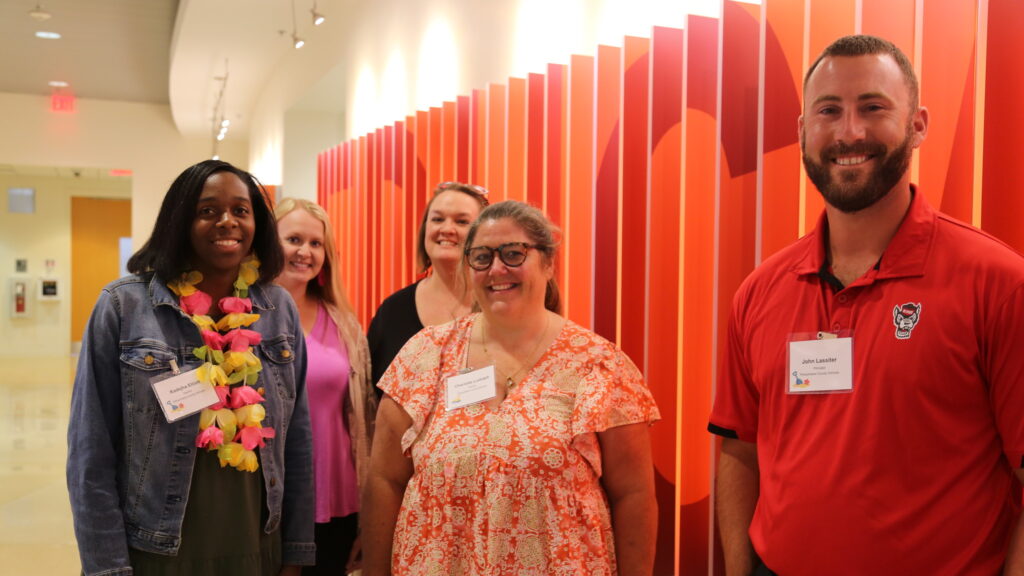 A group of five educators face the camera smiling in front of a red and orange background.