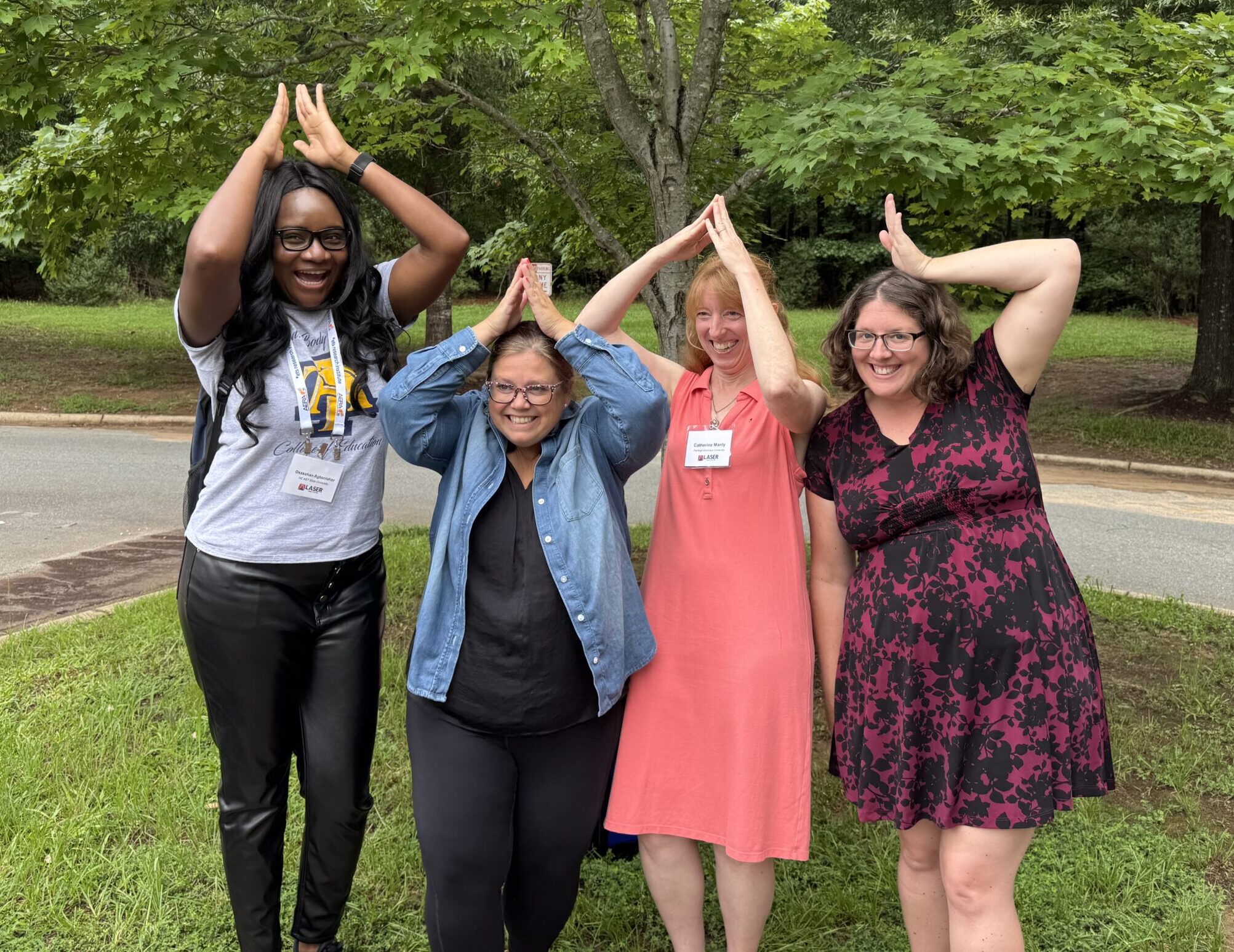 Four women stand in a line and hold their arms in a triangle shape over their heads to illustrate themselves as sharks