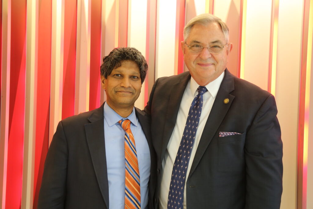 Senators Jay Chaudhuri and Jim Burgin stand beside each other smiling in front of a backlit wall.