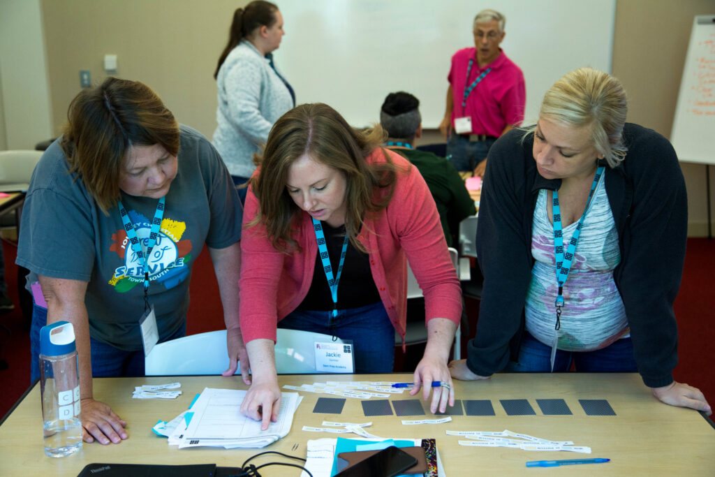 Three educators stand and bend in front of a table working on a project together