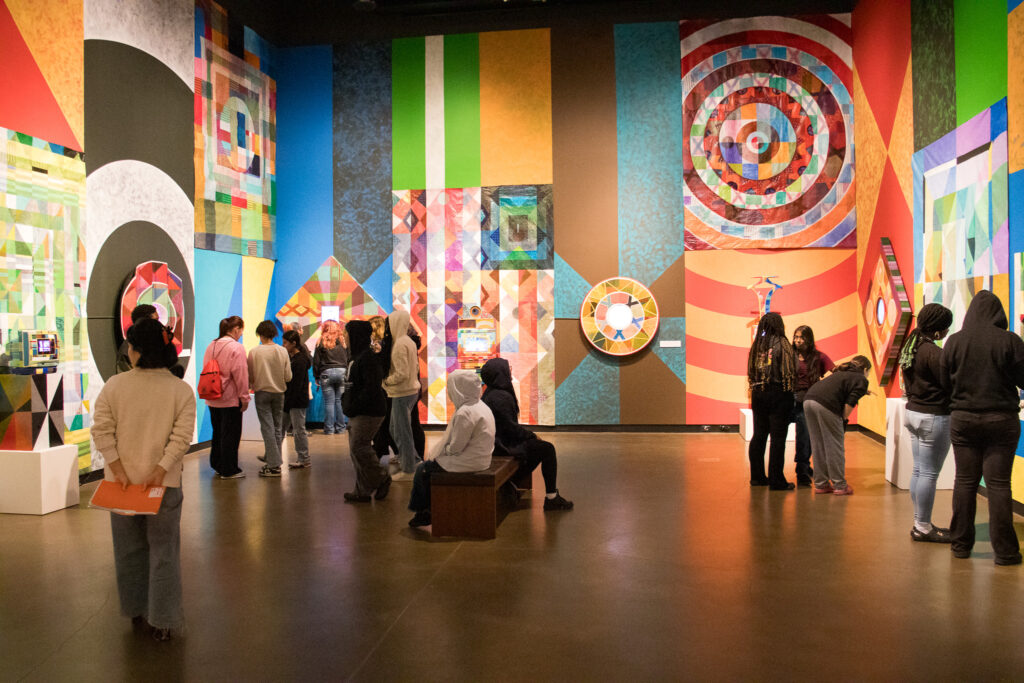 Students visiting an art gallery featuring multicolored patterns, stripes and circles.