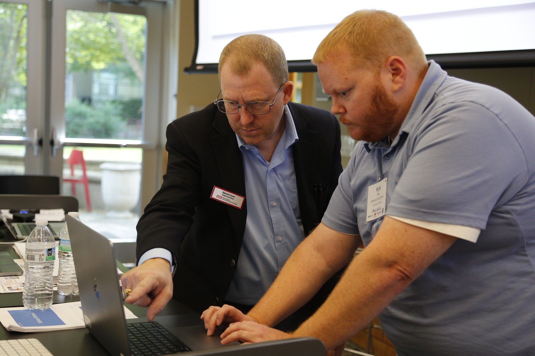 Two men work over a laptop, where one points to the screen guiding the other