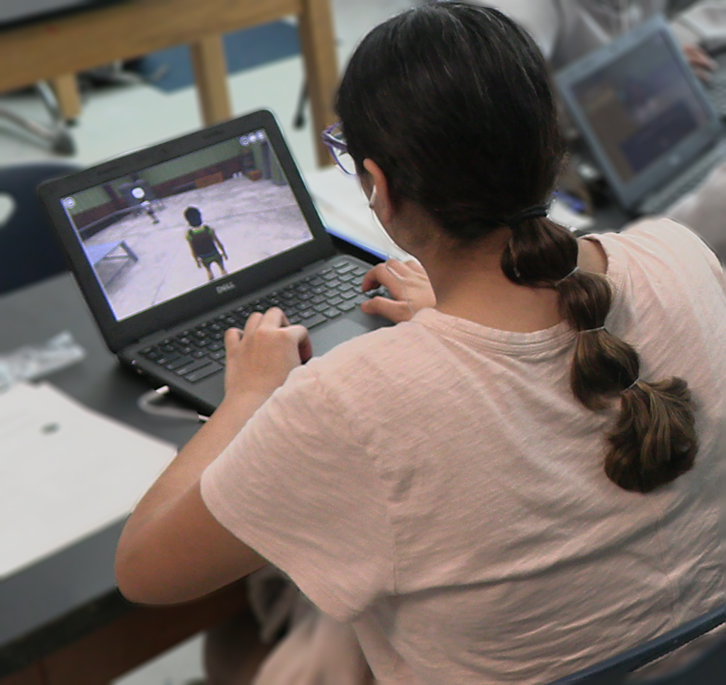 Student sitting at a table playing educational game on laptop
