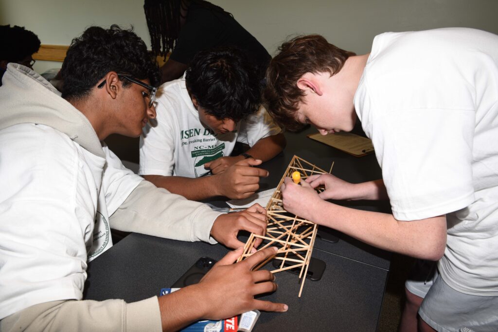 Three students work together at a table building a wooden model.