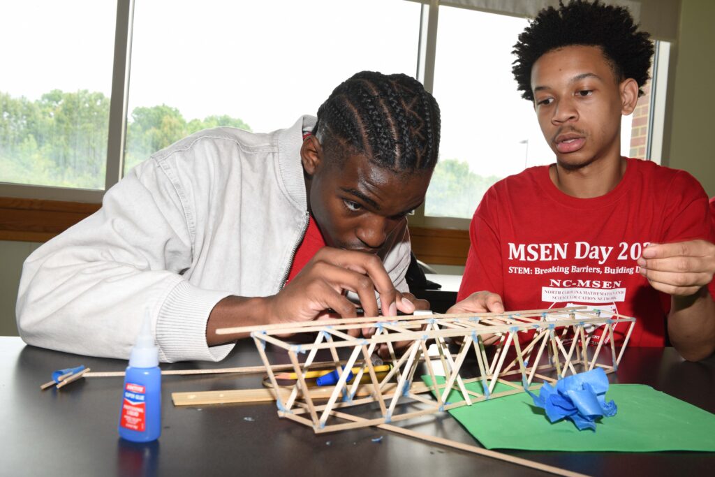 Two students sitting at a table in a classroom building a small scale model.