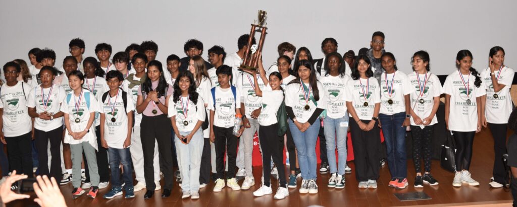A large group of students with a student in the center holding up a trophy.