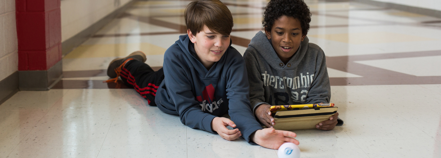 students on floor playing with a ball and using ipad device