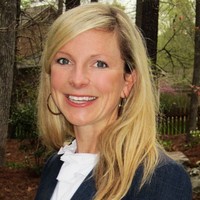 A woman with long blonde hair, a navy blazer and a white ruffled shirt