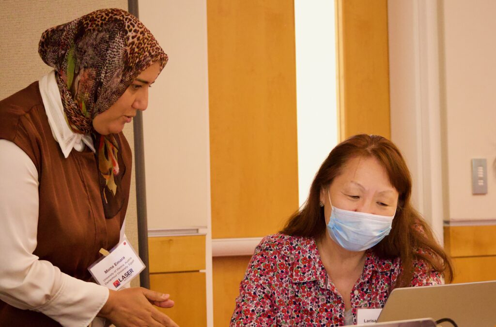 Two researchers work collaboratively. One stands and the other sits as they both look at the computer.