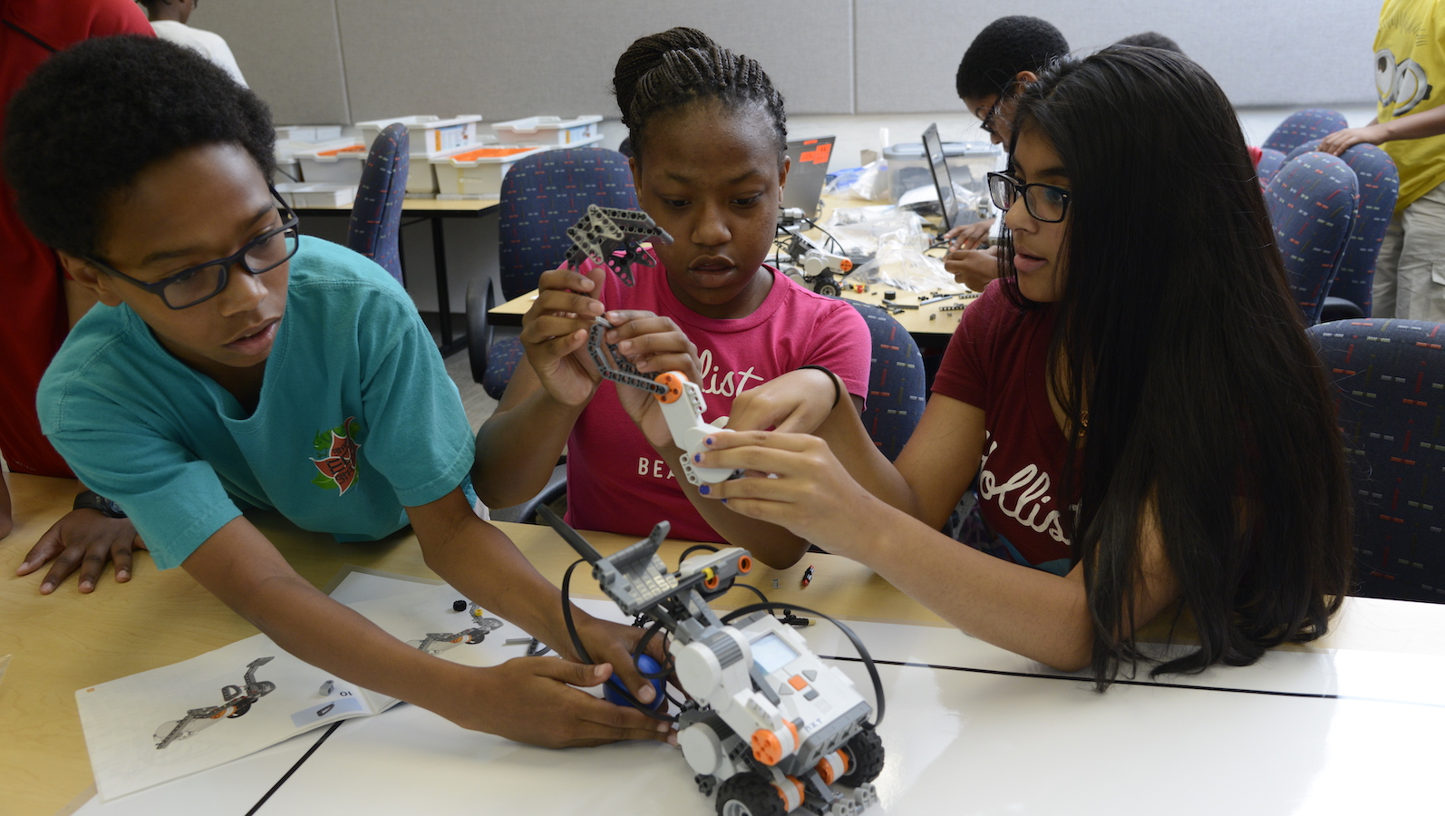 A group of students huddle around a lego robot on a table in a classroom.