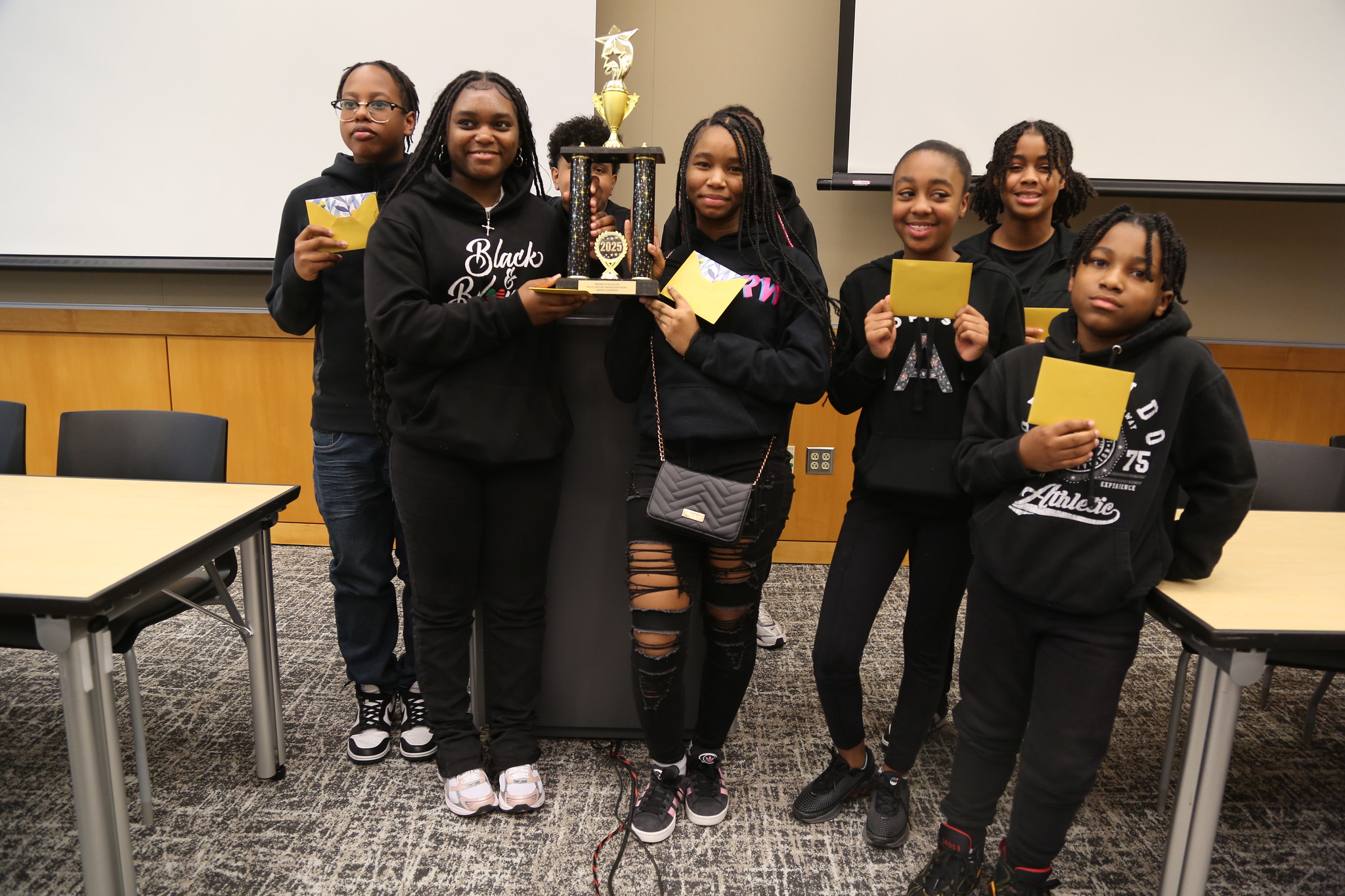 A group of students hold up a trophy and envelopes with prize money in them.