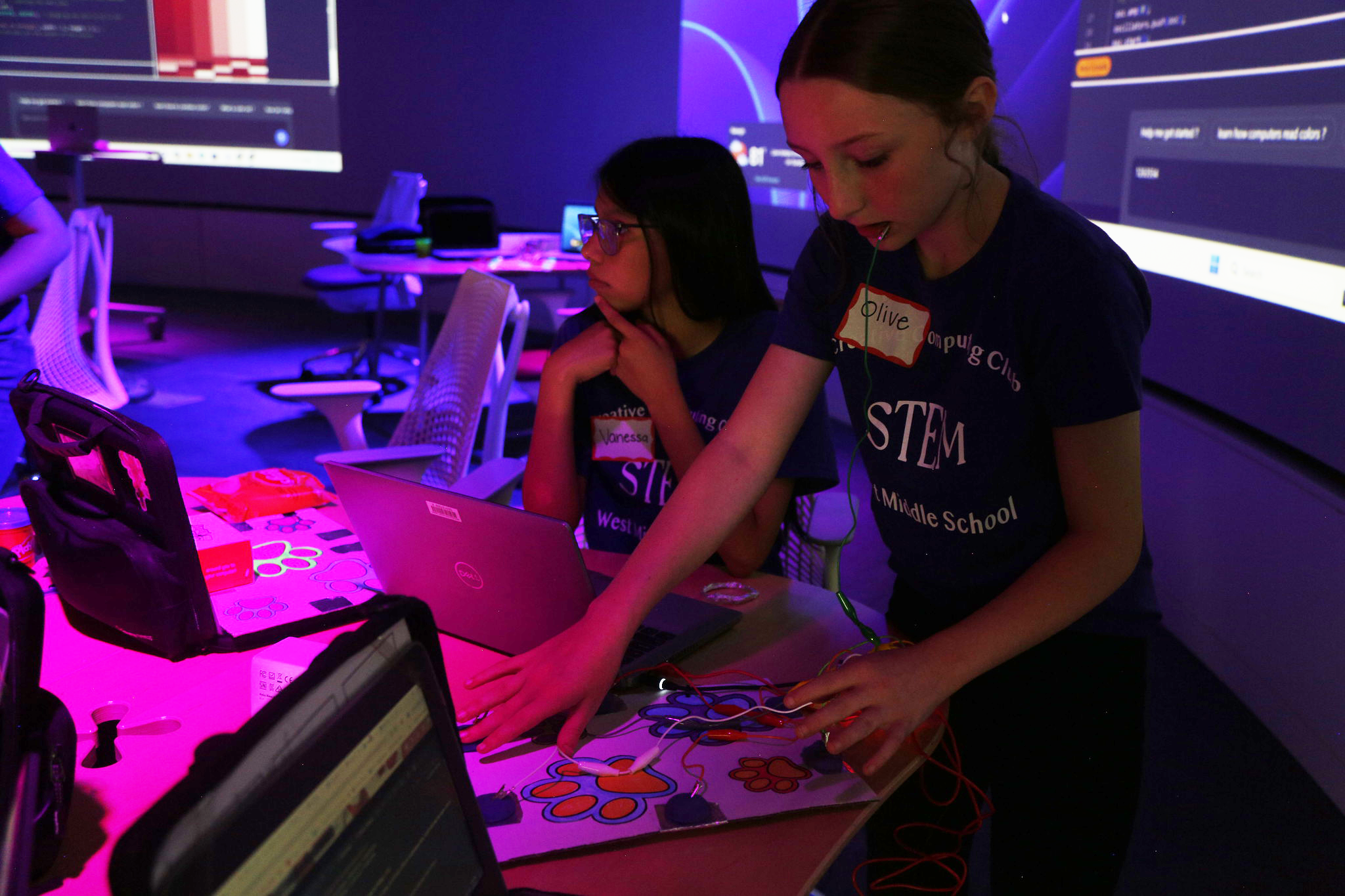 Two girls work on a circuit in a purple illuminated room