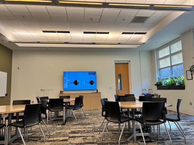 A meeting space with a tv on the wall and round tables with chairs