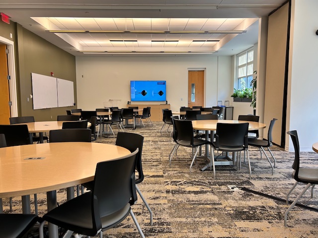 A meeting space with a tv on the wall and round tables with chairs