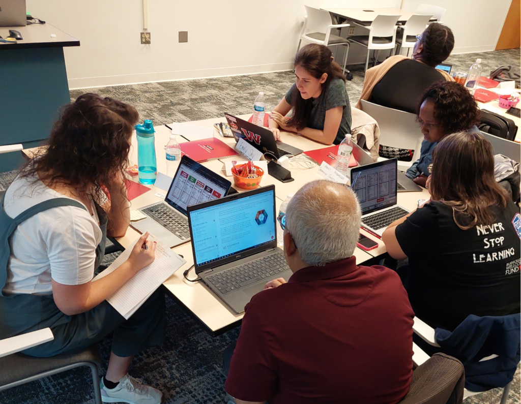 A group of educators sit around a table on laptops