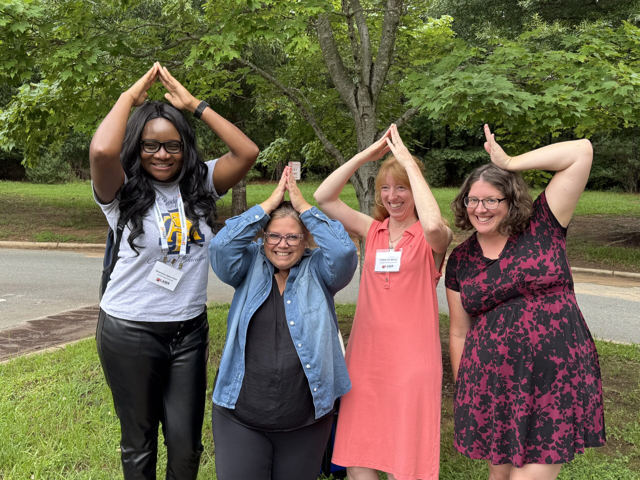 Four women stand in a line holding their arms and hands above their heads to look like shark fins