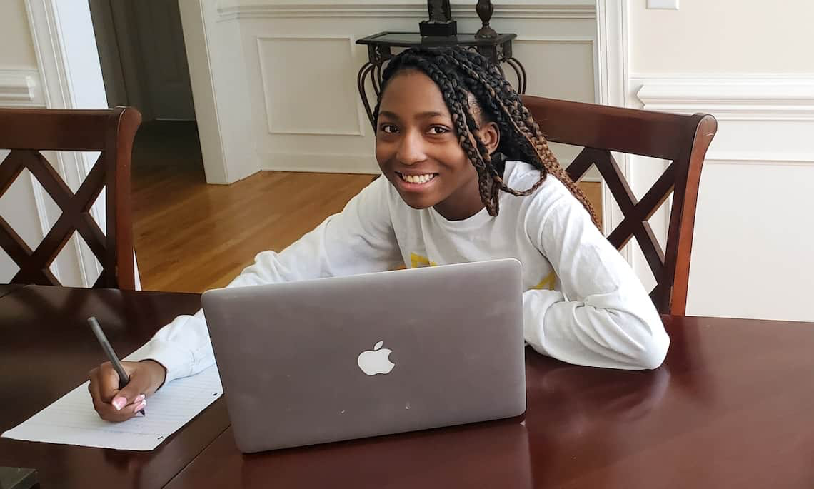 A student works at a table with a paper and laptop