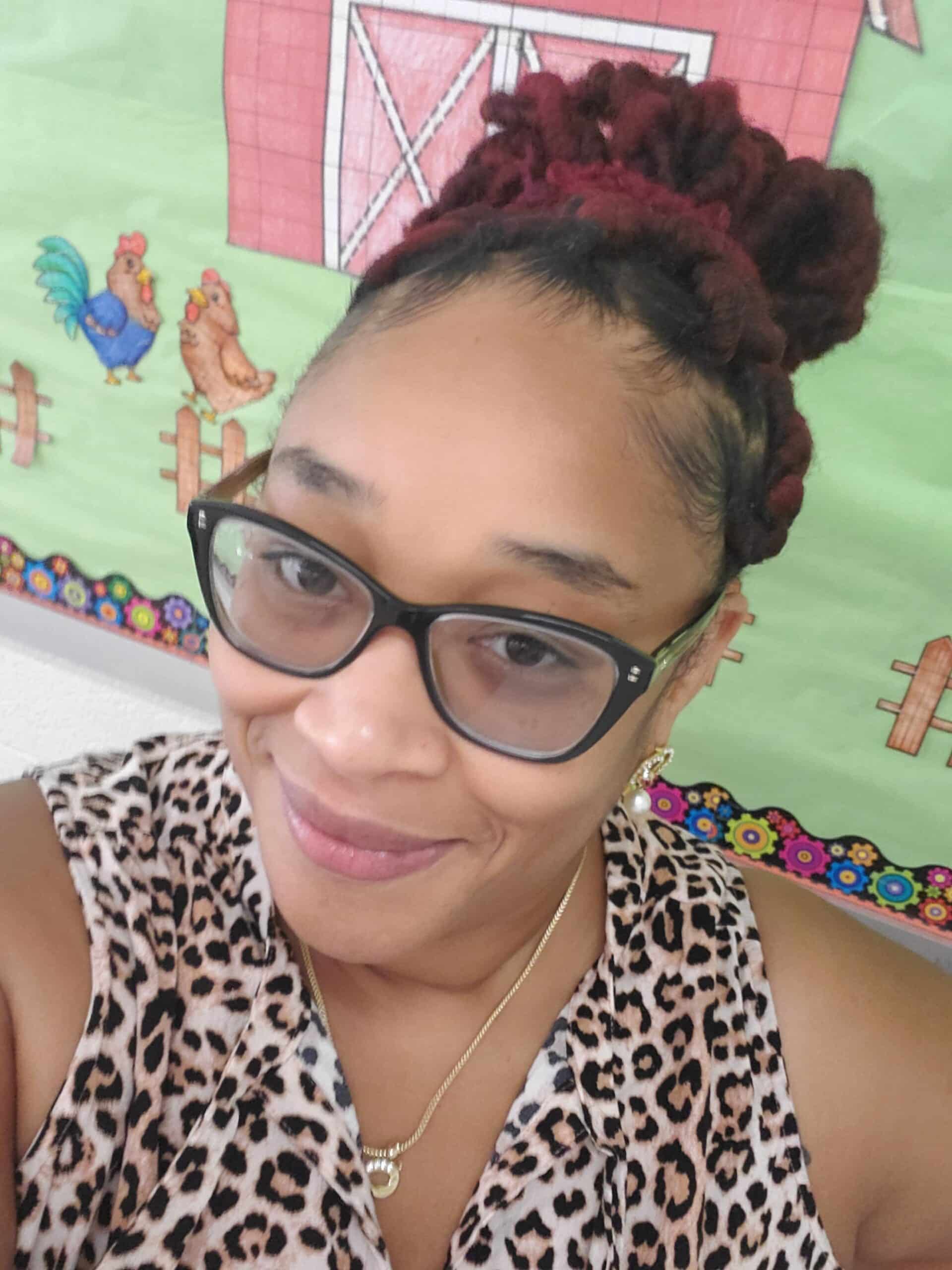 Selfie of a woman with a braided bun, glasses and a leopard print silk top in a classroom