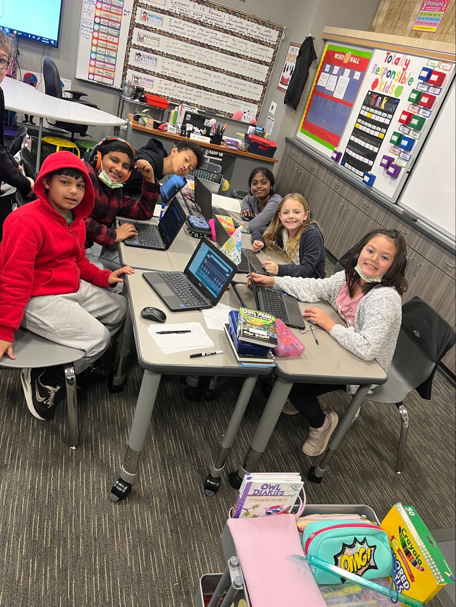 A group of students sit in a classroom at desks with their laptops in front of them.